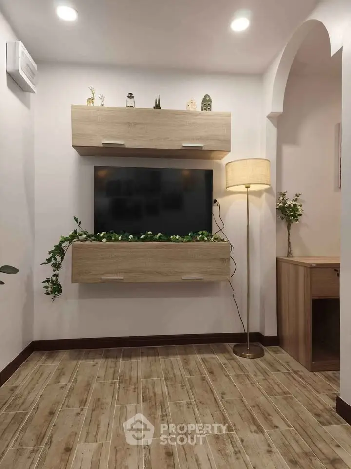 Modern living room with stylish wooden flooring, wall-mounted TV, and elegant lighting.