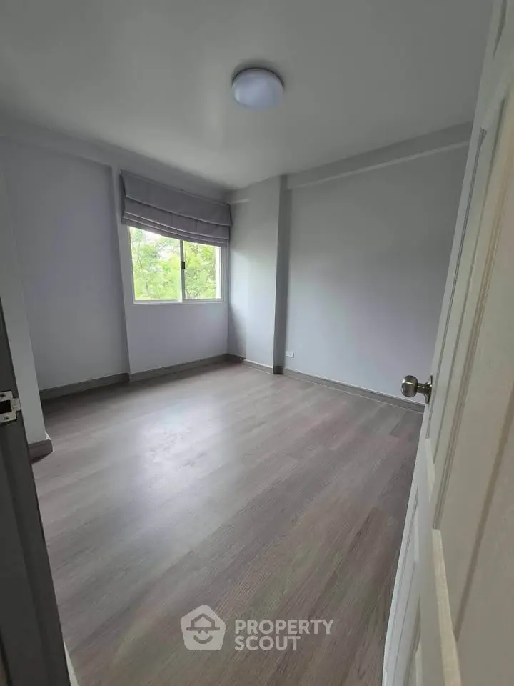 Spacious empty bedroom with large window and wooden flooring