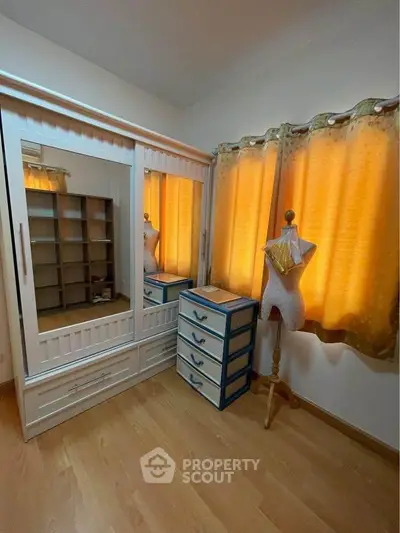 Cozy bedroom with wooden flooring, wardrobe, and mannequin by the window.