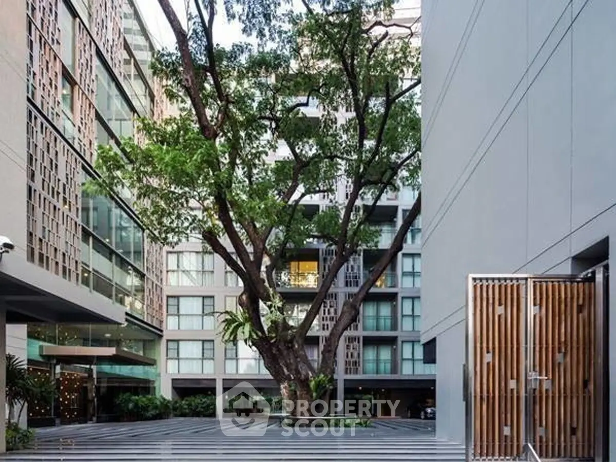 Modern apartment building with lush courtyard and large tree, offering serene urban living.