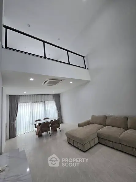Spacious modern living room with high ceiling and mezzanine, featuring elegant furniture and large windows.