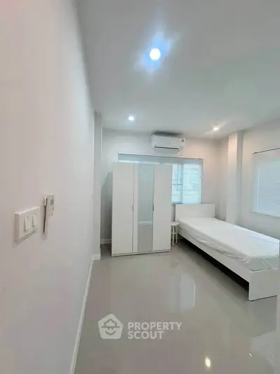 Minimalist bedroom with white furniture and air conditioning in modern apartment.