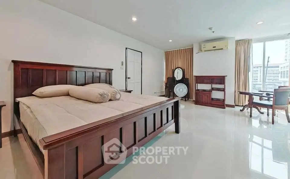 Spacious bedroom with elegant wooden furniture and large windows offering city views.