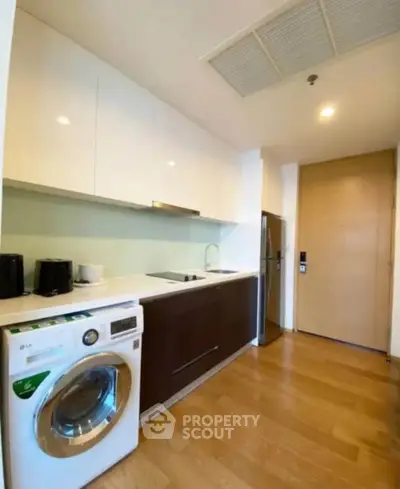 Modern kitchen with sleek cabinets, washing machine, and stainless steel fridge in a compact layout.