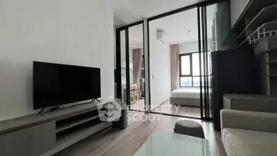 Modern living room with TV and glass partition leading to bedroom, featuring sleek furniture.
