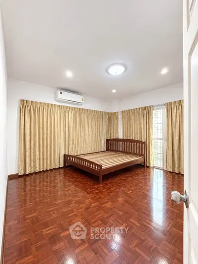Spacious bedroom with wooden flooring and large windows for natural light