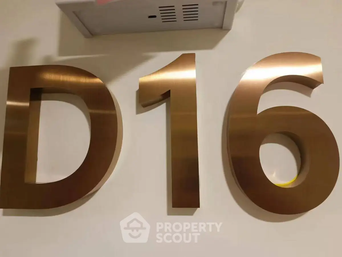 Modern building signage with metallic D16 on a wall, indicating apartment or unit number.