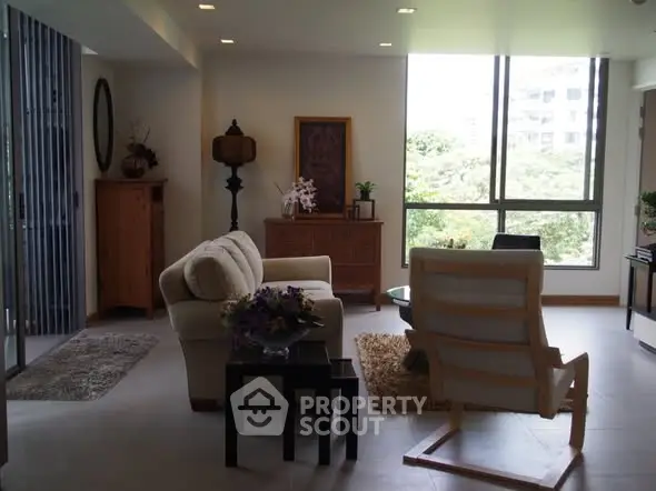 Spacious living room with modern furniture and large window offering natural light and greenery view.