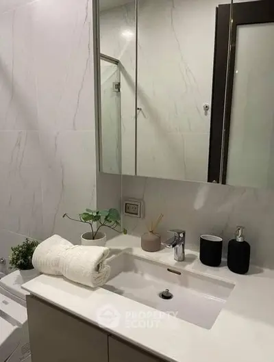 Elegant bathroom with modern fixtures, marble walls, and a sleek vanity unit, complemented by tasteful decor and a large mirror.