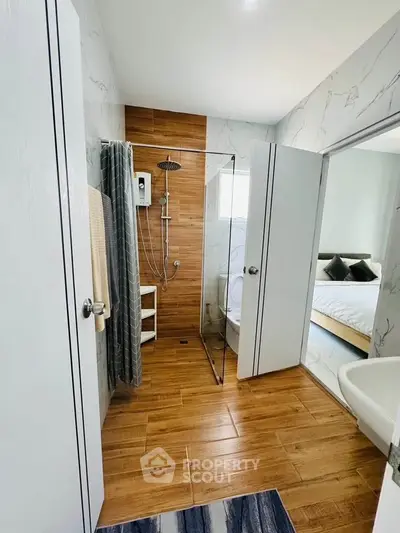 Modern bathroom with glass shower and wooden flooring adjacent to cozy bedroom.