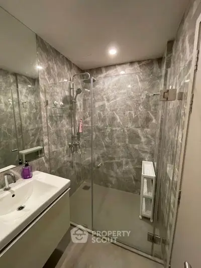 Modern bathroom with glass shower and marble walls, featuring sleek fixtures and ample lighting.