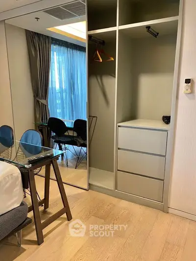 Modern bedroom with built-in wardrobe and glass desk, featuring floor-to-ceiling window with city view.