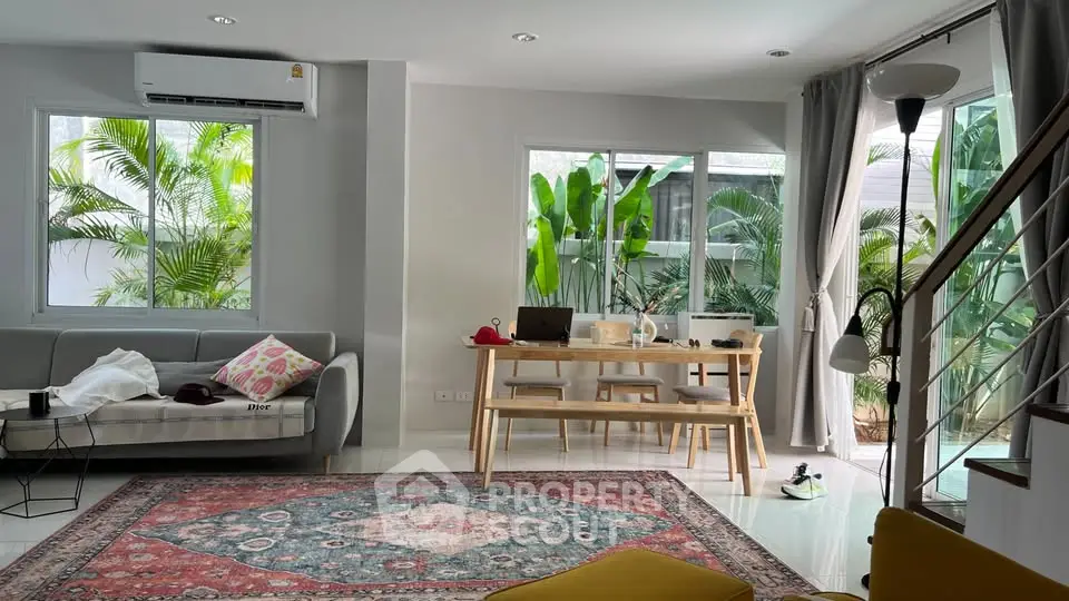 Spacious living room with modern decor and large windows overlooking lush greenery.