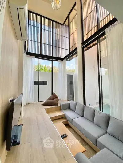Stunning modern living room with high ceilings and large windows, featuring a cozy gray sofa and sleek wooden flooring.