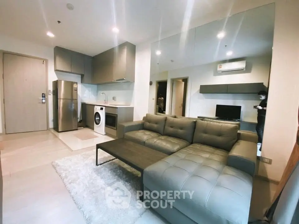 Modern open-plan living room with sleek kitchen, featuring stainless steel appliances and cozy sectional sofa.