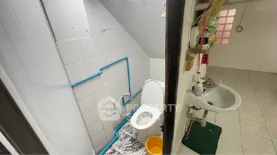 Compact bathroom with white tiles and basic fixtures, featuring a toilet and sink under a sloped ceiling.
