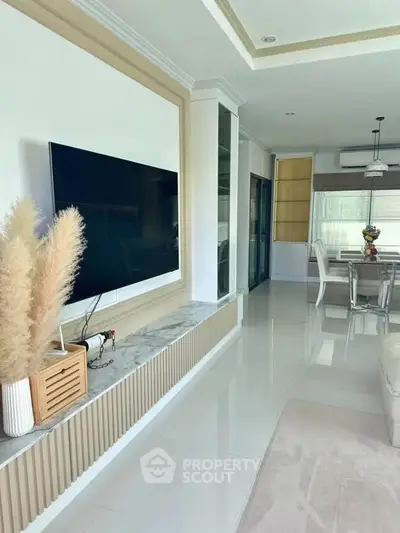 Modern living room with sleek TV setup and elegant dining area, featuring stylish decor and bright natural lighting.