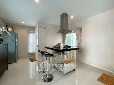 Modern kitchen with sleek island and bar stools, featuring minimalist design and ample natural light.