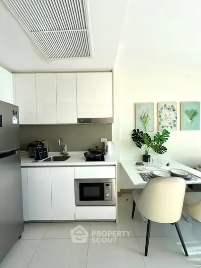 Modern kitchen with sleek white cabinets and dining area, featuring built-in microwave and elegant decor.