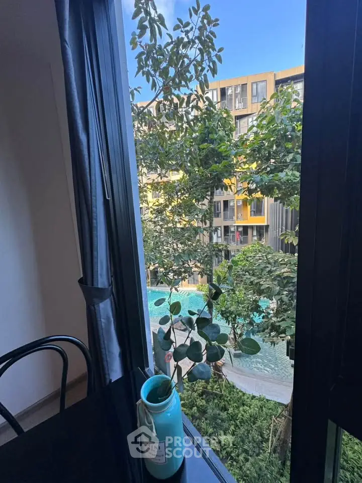 Stunning view from window overlooking modern building and lush greenery with pool.
