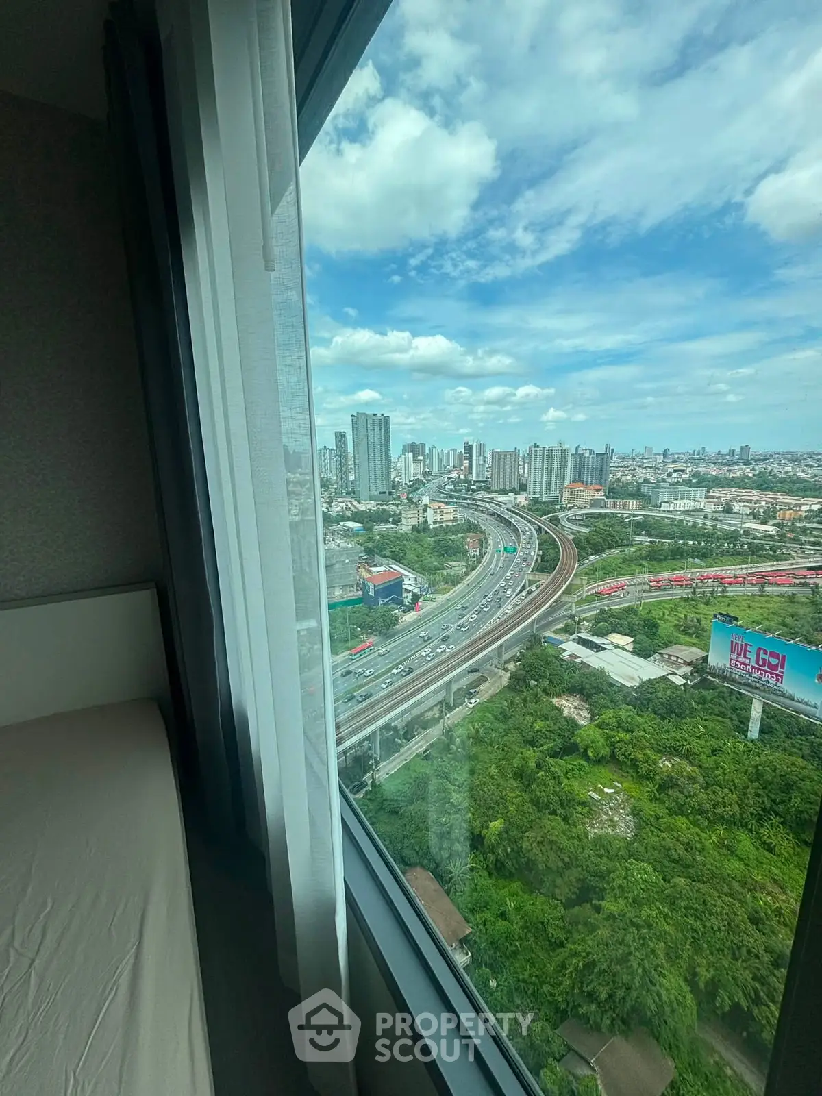 Stunning cityscape view from high-rise apartment window with lush greenery and urban skyline.
