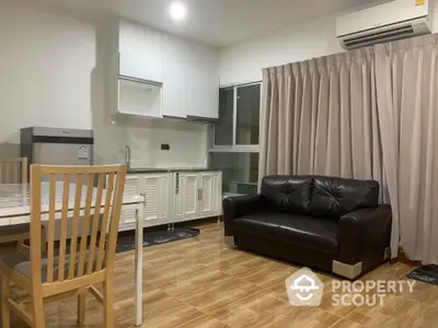 Modern living room with sleek kitchen, featuring a black leather sofa and wooden dining set, perfect for cozy gatherings.