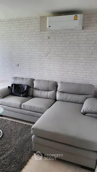 Modern living room with stylish gray sectional sofa and air conditioning, perfect for comfort and relaxation.