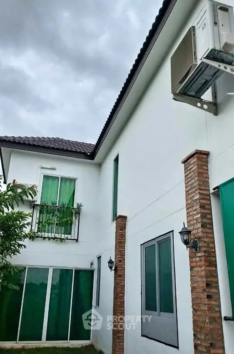 Modern two-story house exterior with brick columns and green accents under cloudy sky.
