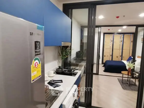Modern apartment kitchen with sleek appliances and view into cozy bedroom.