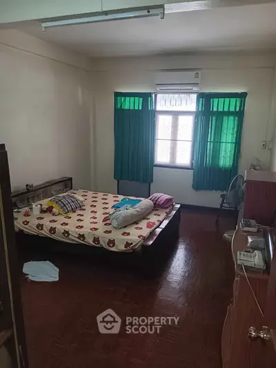 Cozy bedroom with wooden flooring and natural light through green curtains.