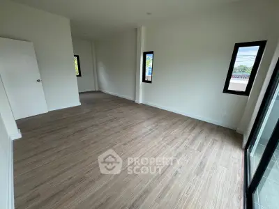 Spacious empty room with wooden flooring and large windows offering natural light.