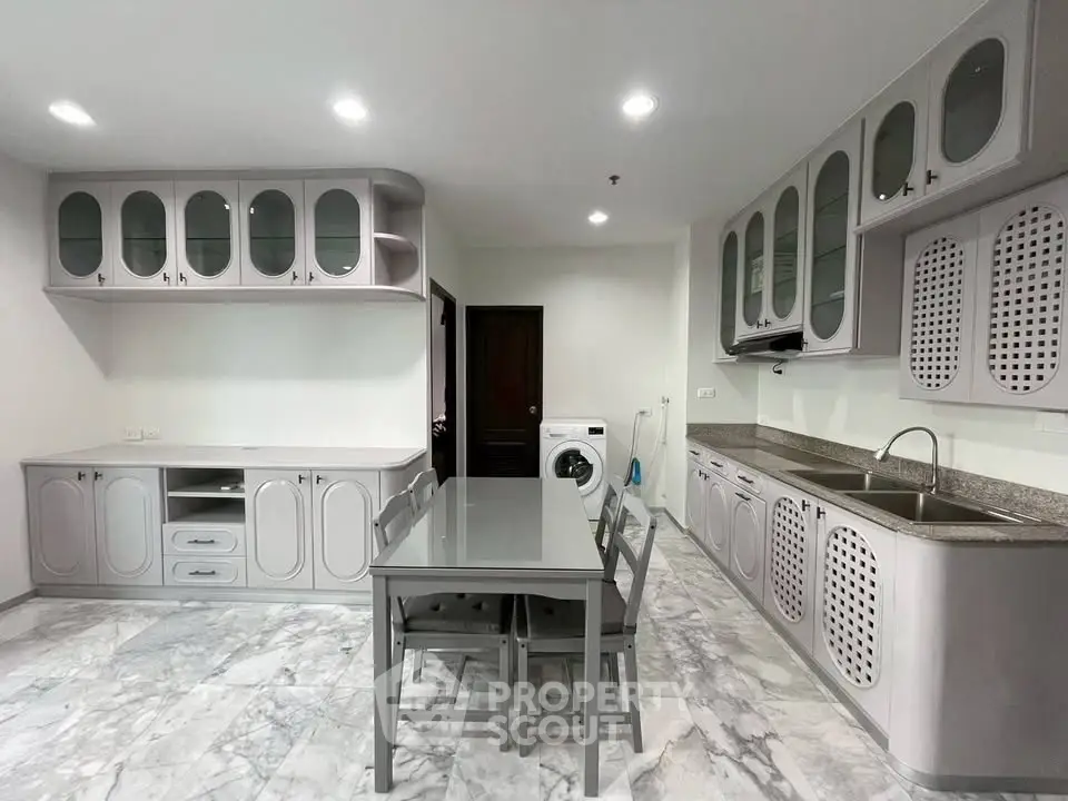 Spacious kitchen with modern cabinetry and dining area, featuring marble flooring and integrated washing machine.