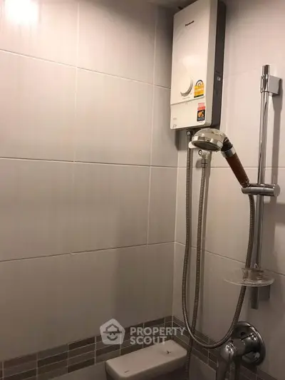 Compact bathroom with modern shower and water heater in sleek tiled design.