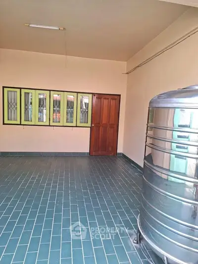 Spacious tiled area with stainless steel water tank and wooden door, ideal for storage or utility use.