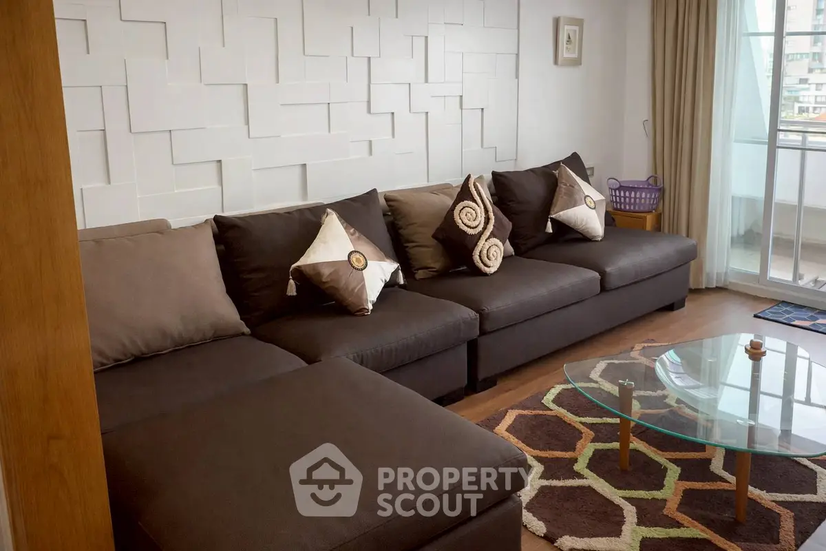 Stylish living room with modern sectional sofa and geometric glass coffee table, featuring a balcony view.