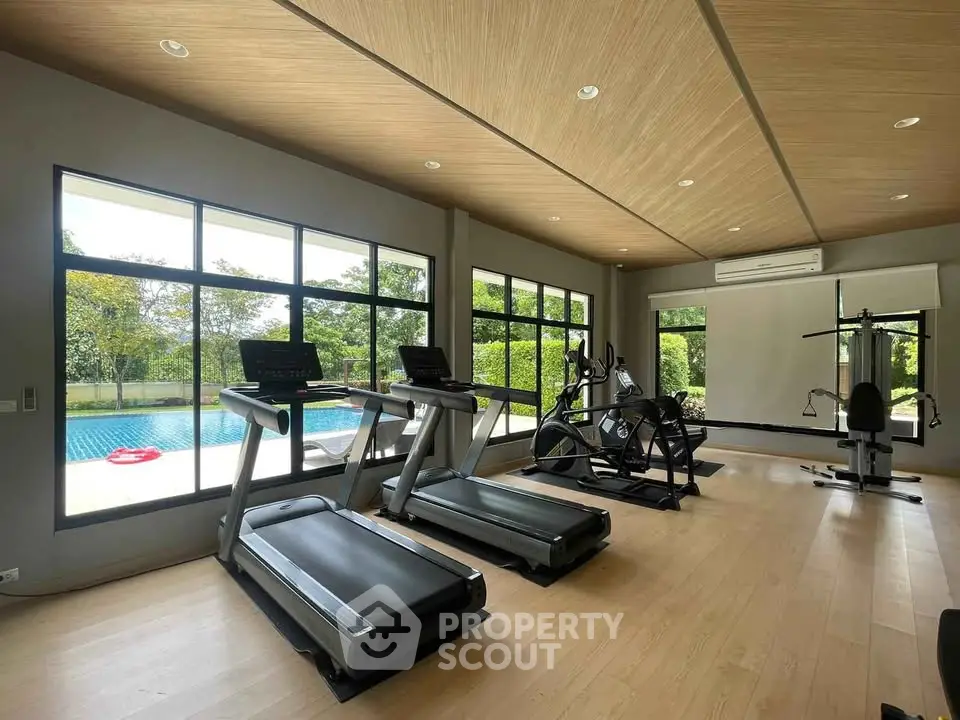 Modern gym with large windows overlooking a pool, featuring state-of-the-art exercise equipment.