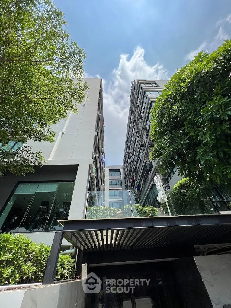 Modern building exterior with lush greenery and glass balcony under a clear blue sky.