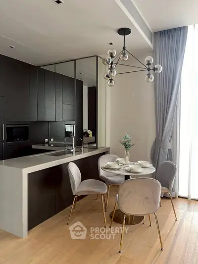 Modern kitchen with sleek black cabinets, open layout, and elegant dining area with stylish chandelier.