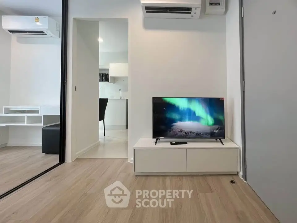 Modern living room with sleek TV setup and air conditioning, adjacent to a stylish kitchen.