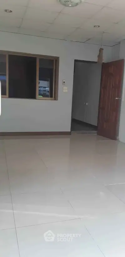 Spacious empty room with tiled flooring and wooden door, ideal for customization.