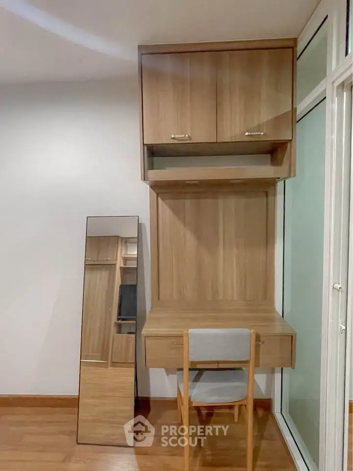 Modern study nook with wooden desk, chair, and mirror in a bright room.