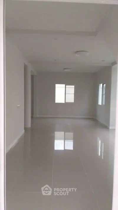 Spacious empty room with glossy tiled flooring and large windows for natural light.