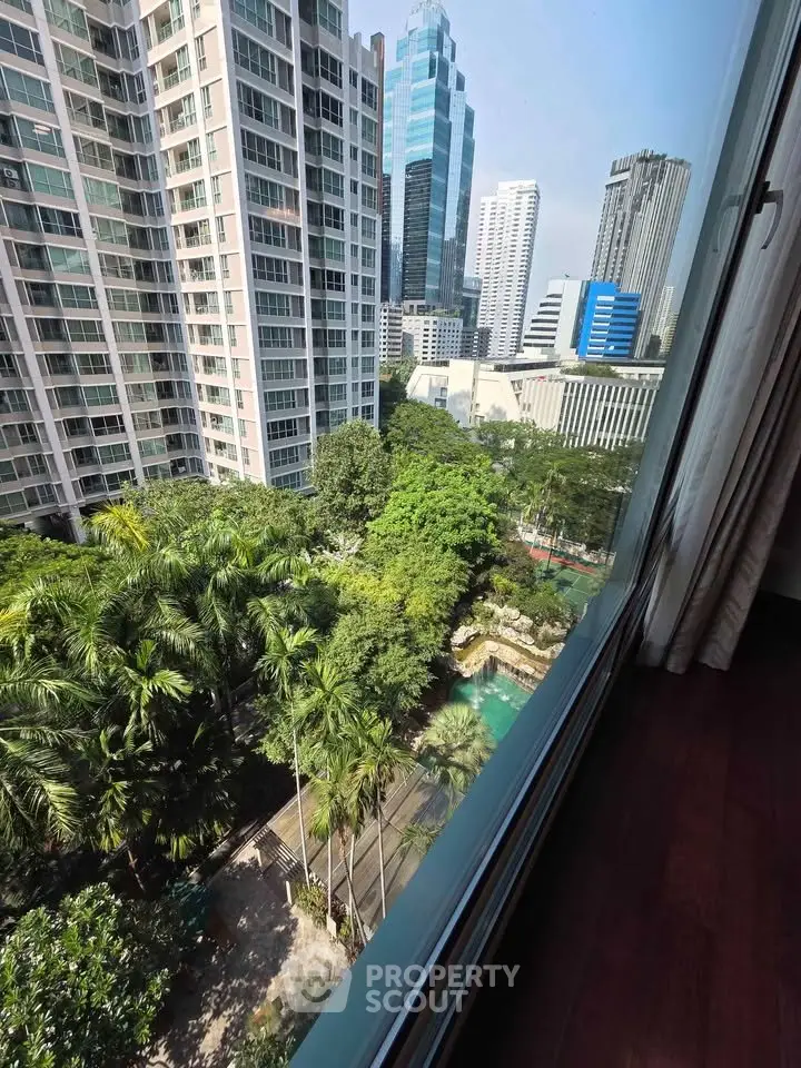 Stunning cityscape view from high-rise apartment window overlooking lush greenery and modern skyscrapers.