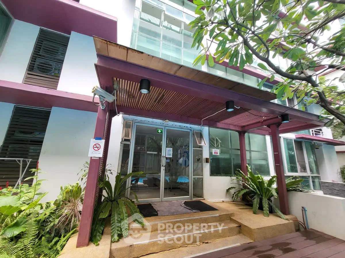 Modern building entrance with glass doors and lush greenery, showcasing contemporary architecture and inviting ambiance.