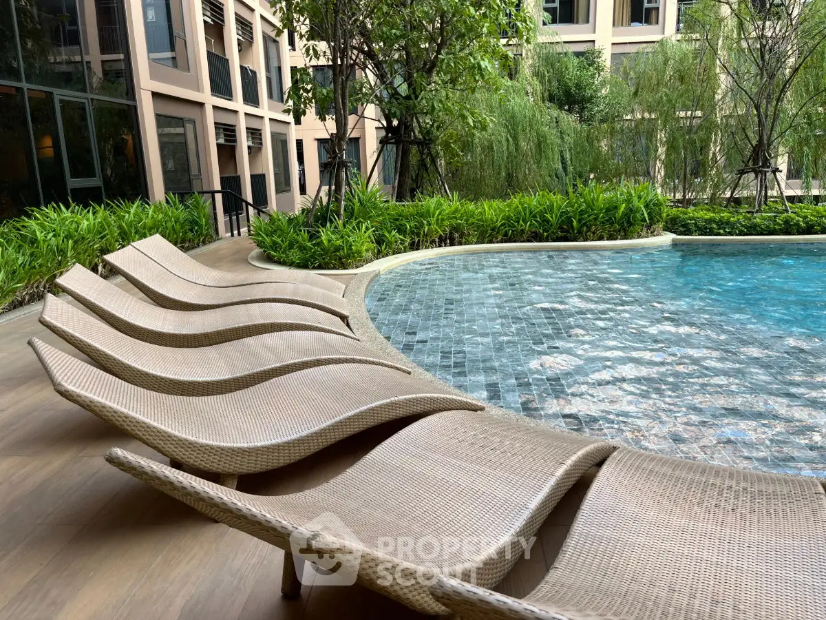 Luxurious poolside area with stylish loungers and lush greenery in modern residential complex.