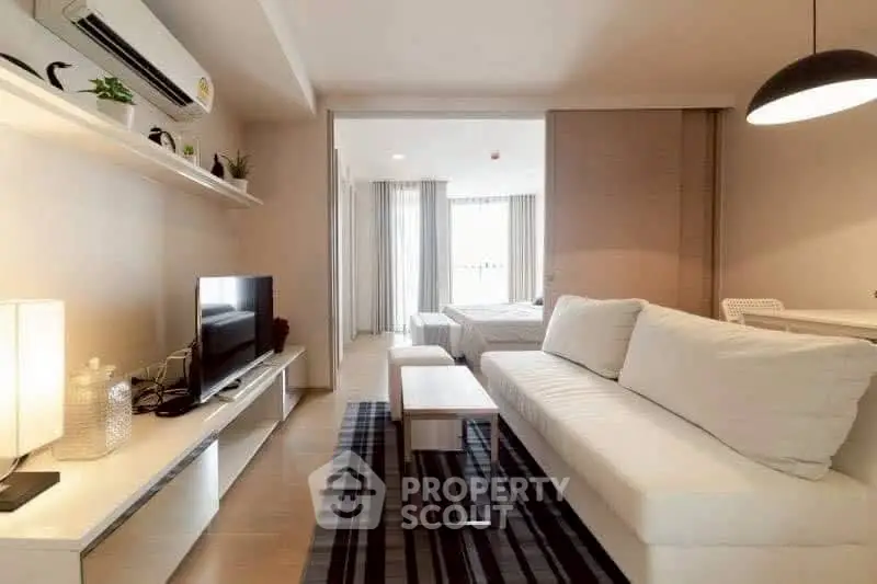 Modern living room with sleek furniture and open layout leading to a cozy bedroom.