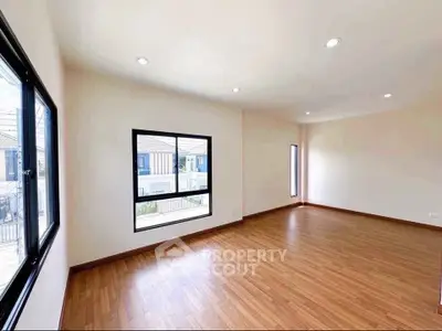 Spacious empty room with wooden flooring and large windows offering natural light.