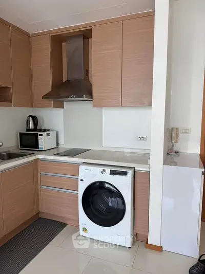 Modern kitchen with wooden cabinets, washing machine, and stainless steel appliances.