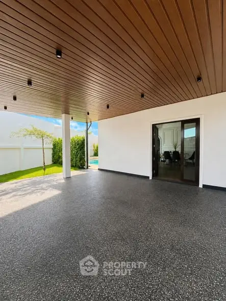 Spacious modern patio with wooden ceiling and garden view, perfect for outdoor gatherings.