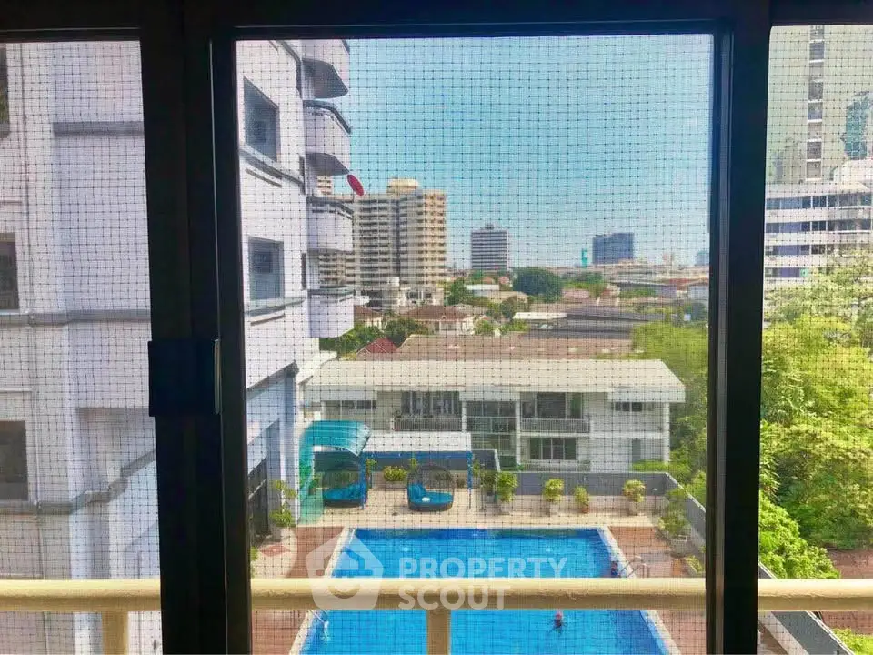 Stunning city view from a high-rise apartment overlooking a sparkling pool and lush greenery.